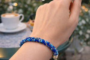 Handmade blue Kumihimo bracelet worn at café table, Caribbean Blue glass seed beads, adjustable clasp artisan jewelry